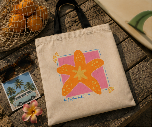 Psalm 148:7 starfish graphic tote bag photographed on a rustic wooden table with relaxed beach-inspired styling and warm vintage lighting.