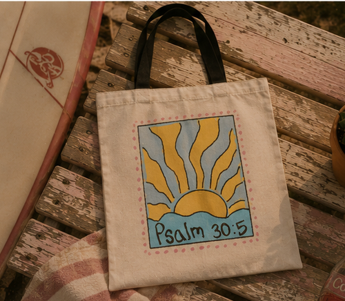 Psalm 30:5 sunrise graphic tote bag photographed on a rustic wooden bench with warm vintage beach-inspired styling.