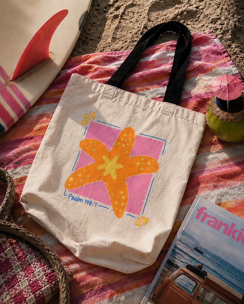 Faith-inspired Psalm 148:7 starfish tote bag photographed on a colorful beach towel beside a surfboard in warm coastal sunset lighting.